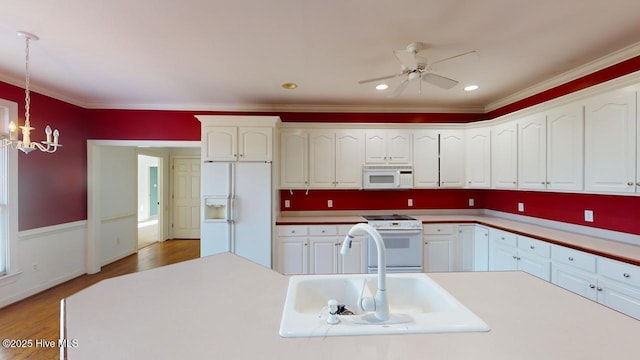 kitchen with white appliances, sink, wood-type flooring, white cabinetry, and hanging light fixtures