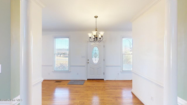 foyer entrance featuring light hardwood / wood-style floors, ornamental molding, and a chandelier