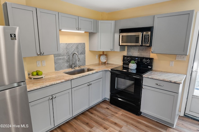 kitchen featuring light wood-style flooring, a sink, stainless steel appliances, decorative backsplash, and gray cabinetry