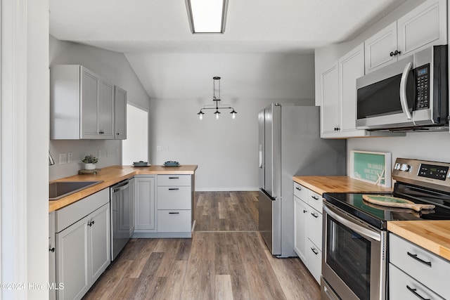 kitchen featuring pendant lighting, hardwood / wood-style floors, lofted ceiling, appliances with stainless steel finishes, and butcher block countertops