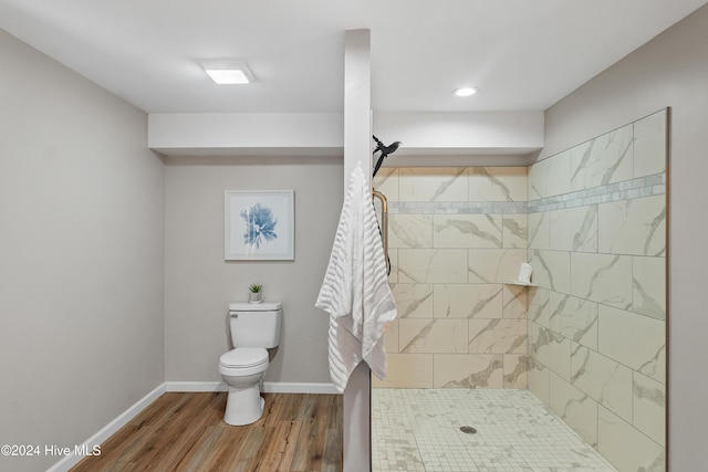 full bath with tiled shower, baseboards, toilet, and wood finished floors