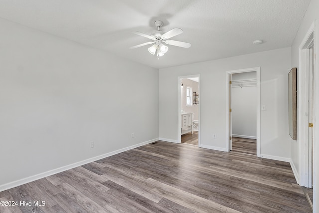 unfurnished bedroom with ensuite bath, ceiling fan, a spacious closet, wood-type flooring, and a closet