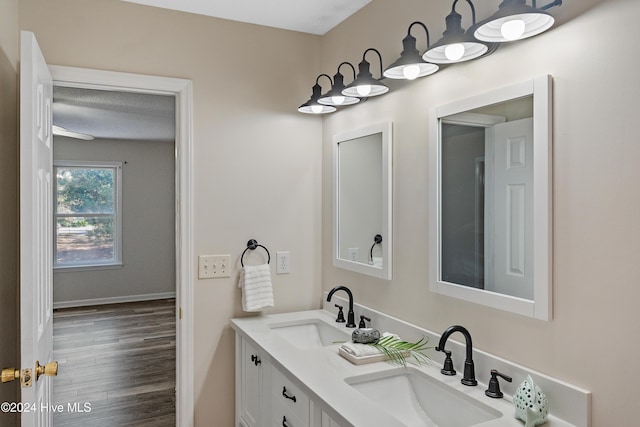 bathroom with double vanity, baseboards, a sink, and wood finished floors