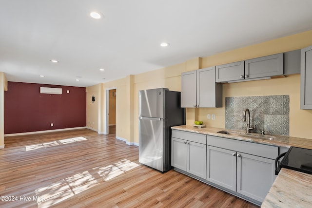 kitchen with freestanding refrigerator, light wood-type flooring, a sink, gray cabinetry, and backsplash
