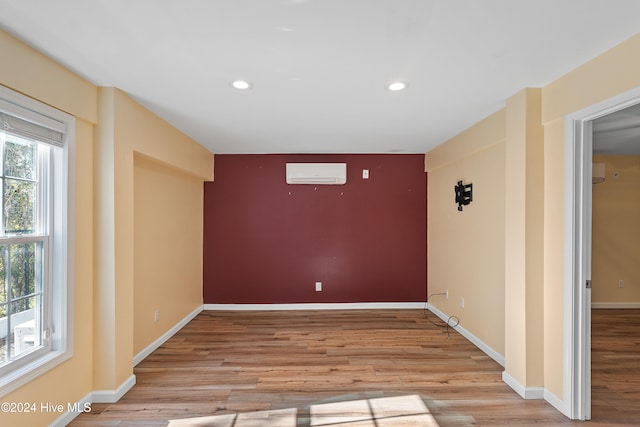 unfurnished room with a wall unit AC, plenty of natural light, and light hardwood / wood-style floors