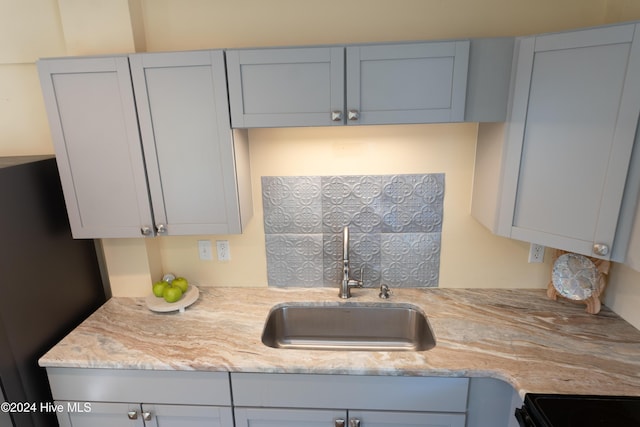kitchen with a sink, freestanding refrigerator, and light stone counters