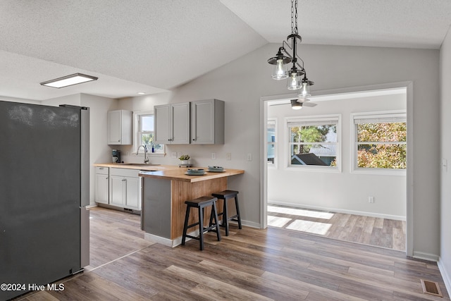 kitchen with a textured ceiling, freestanding refrigerator, a breakfast bar area, lofted ceiling, and a sink