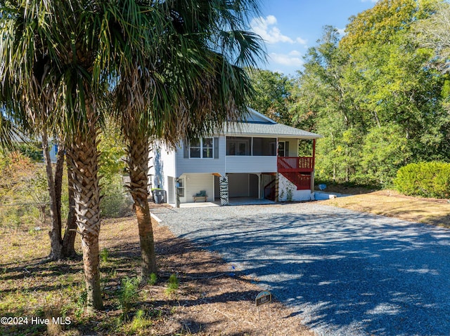 view of front facade with a carport, a sunroom, and gravel driveway