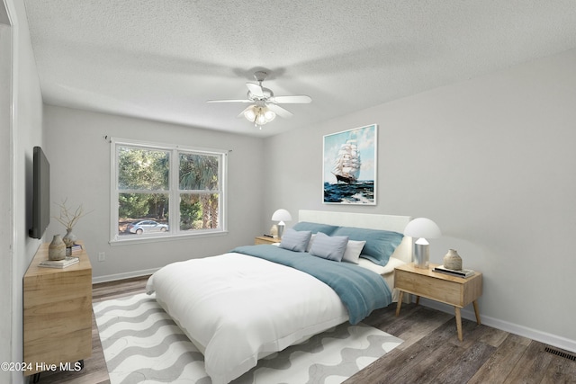 bedroom featuring visible vents, baseboards, a ceiling fan, a textured ceiling, and wood finished floors
