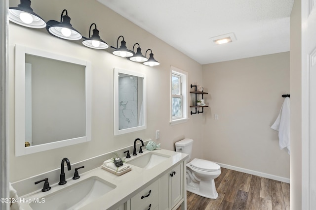 full bath with double vanity, a sink, toilet, and wood finished floors
