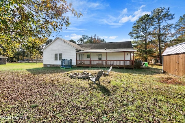 rear view of property featuring a storage shed, a wooden deck, a fire pit, a yard, and a trampoline