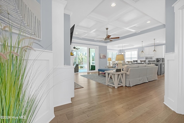 living room with coffered ceiling, ceiling fan, light wood-type flooring, ornamental molding, and beamed ceiling