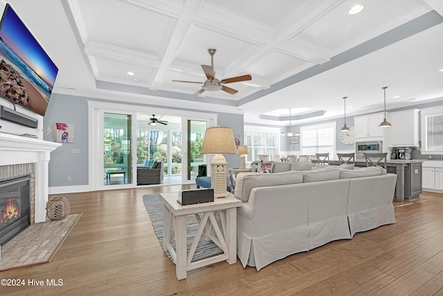 living room with coffered ceiling, ceiling fan, light hardwood / wood-style floors, and a brick fireplace