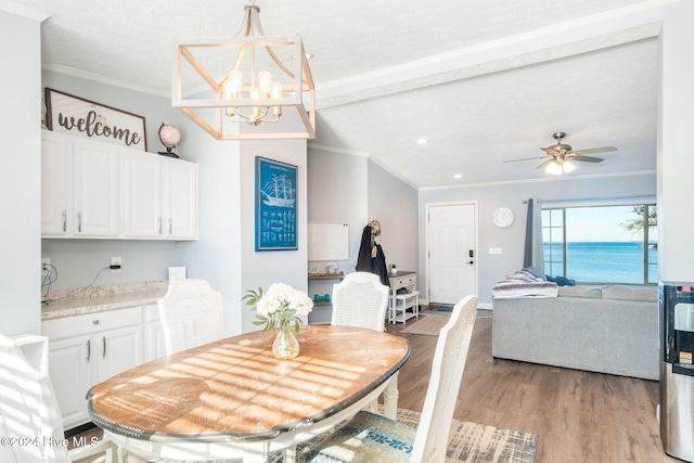 dining room with light hardwood / wood-style floors, a textured ceiling, a water view, ceiling fan with notable chandelier, and ornamental molding