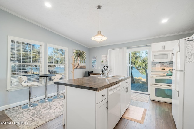 kitchen featuring white appliances, a center island with sink, sink, hanging light fixtures, and white cabinetry