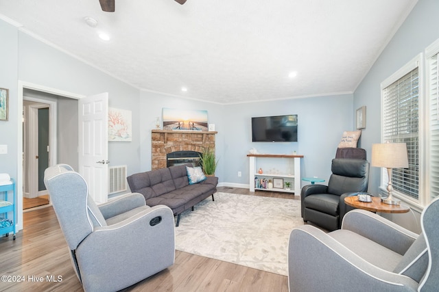 living room featuring hardwood / wood-style floors, a stone fireplace, ceiling fan, and crown molding