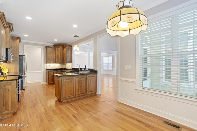 kitchen featuring sink, hanging light fixtures, ornamental molding, appliances with stainless steel finishes, and light hardwood / wood-style floors