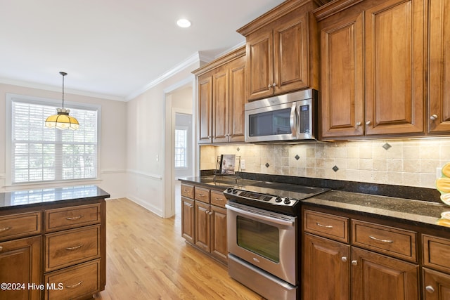 kitchen with dark stone counters, decorative backsplash, ornamental molding, appliances with stainless steel finishes, and light hardwood / wood-style floors