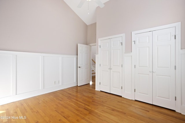 unfurnished bedroom with ceiling fan, light hardwood / wood-style flooring, high vaulted ceiling, and two closets