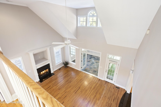 unfurnished living room featuring wood-type flooring, ceiling fan, and a high ceiling