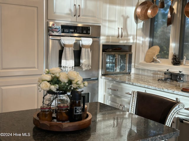 kitchen with white cabinetry, stone countertops, double oven, and a wealth of natural light