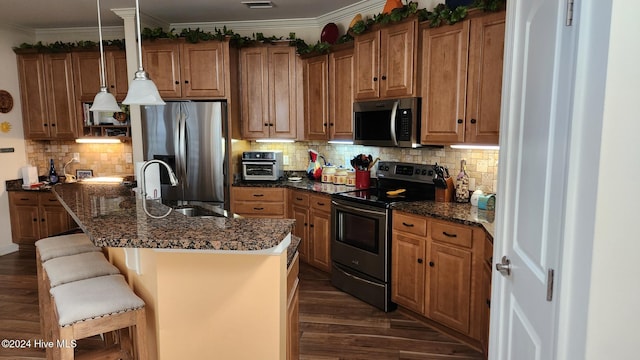 kitchen featuring stainless steel appliances, dark hardwood / wood-style floors, decorative light fixtures, a kitchen bar, and a kitchen island with sink