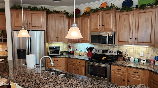 kitchen with sink, hanging light fixtures, dark stone counters, appliances with stainless steel finishes, and ornamental molding