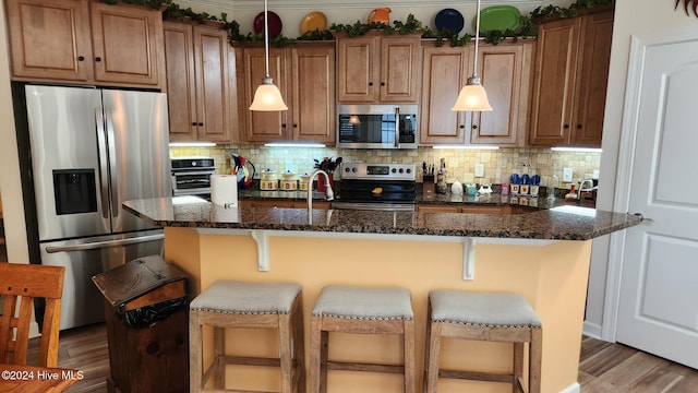 kitchen featuring a kitchen breakfast bar, dark hardwood / wood-style flooring, dark stone countertops, and appliances with stainless steel finishes