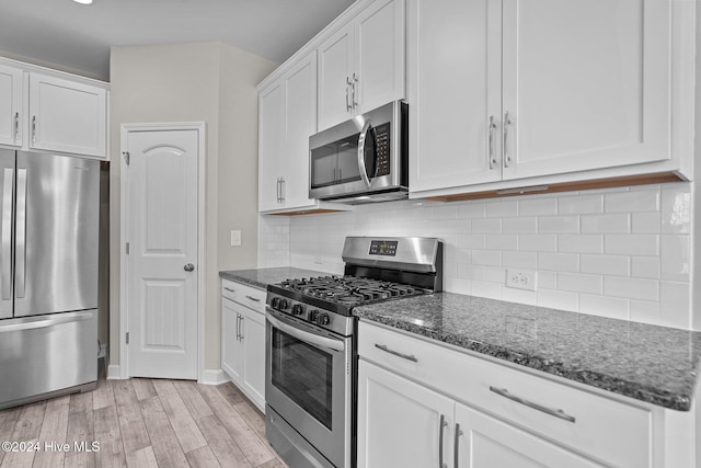 kitchen with dark stone counters, white cabinets, stainless steel appliances, and light hardwood / wood-style floors