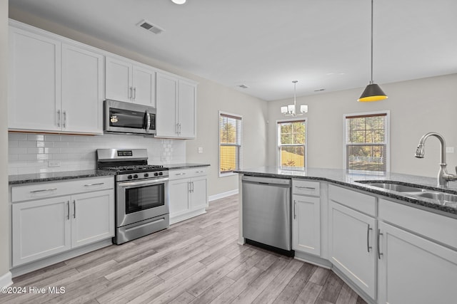 kitchen with appliances with stainless steel finishes, sink, decorative light fixtures, light hardwood / wood-style flooring, and white cabinets