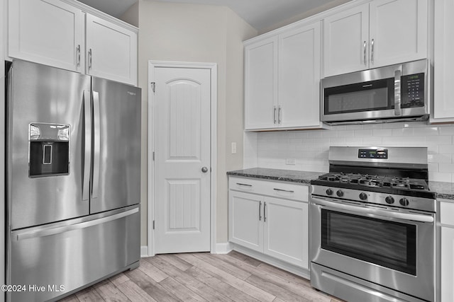 kitchen with appliances with stainless steel finishes, tasteful backsplash, dark stone counters, light hardwood / wood-style flooring, and white cabinetry