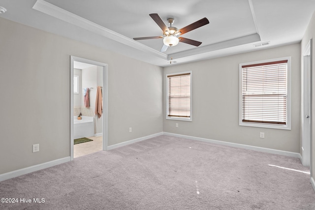 unfurnished bedroom featuring a tray ceiling, multiple windows, ensuite bathroom, and ornamental molding