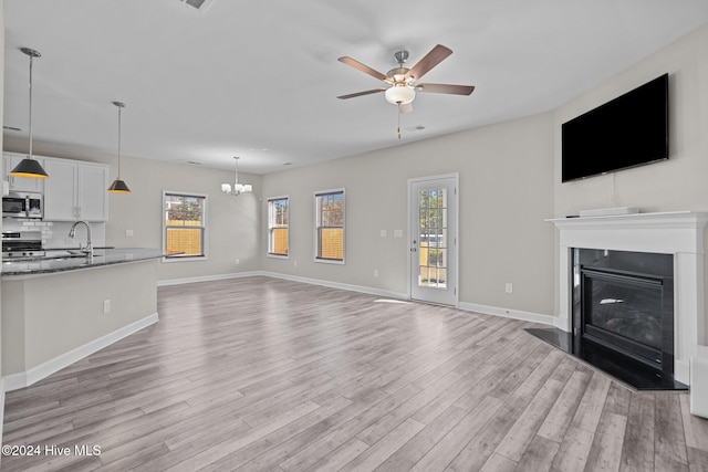 unfurnished living room with ceiling fan with notable chandelier, light wood-type flooring, sink, and a wealth of natural light