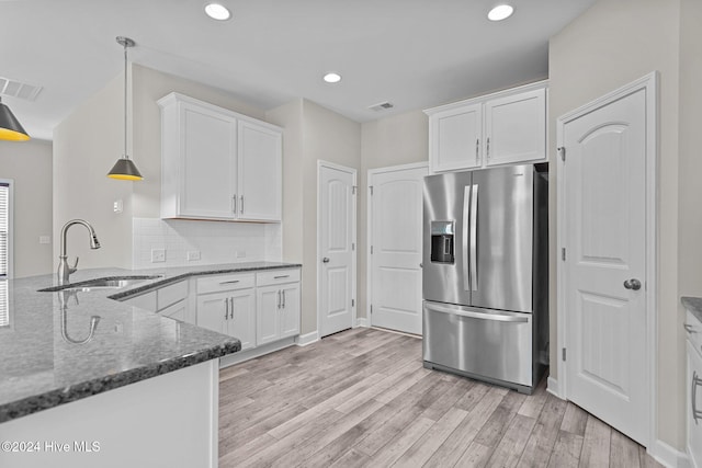 kitchen featuring sink, hanging light fixtures, stainless steel fridge, light hardwood / wood-style floors, and white cabinets