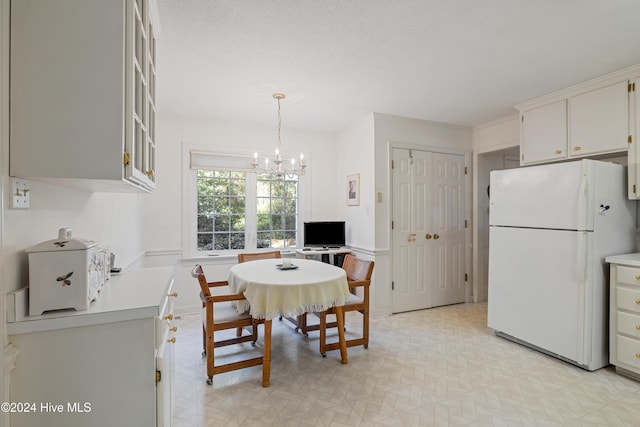 kitchen with a textured ceiling, white refrigerator, decorative light fixtures, an inviting chandelier, and white cabinetry