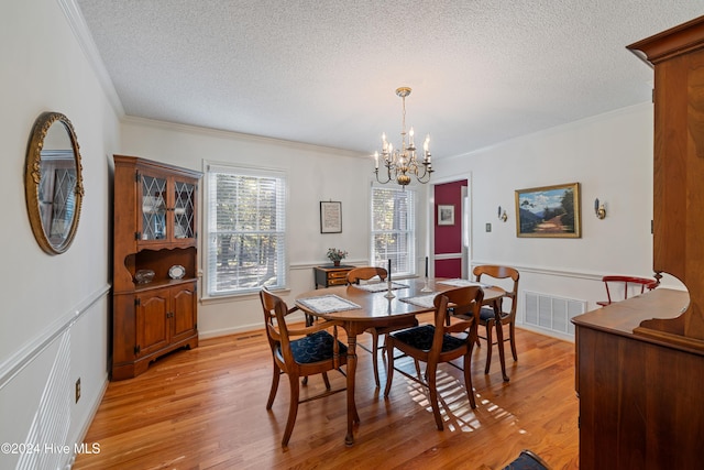 dining space with a textured ceiling, light wood-type flooring, ornamental molding, and a notable chandelier