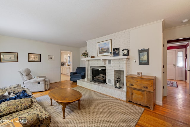 living room with light hardwood / wood-style floors, a brick fireplace, and ornamental molding