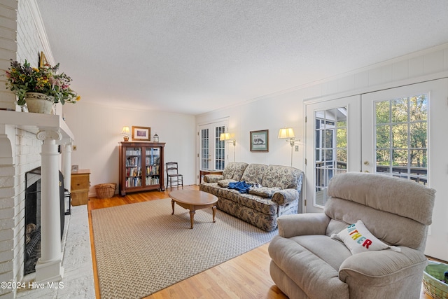 living room featuring hardwood / wood-style floors, a textured ceiling, a brick fireplace, and french doors