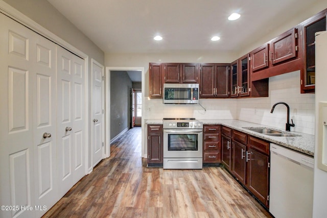 kitchen with light stone countertops, sink, stainless steel appliances, backsplash, and light wood-type flooring