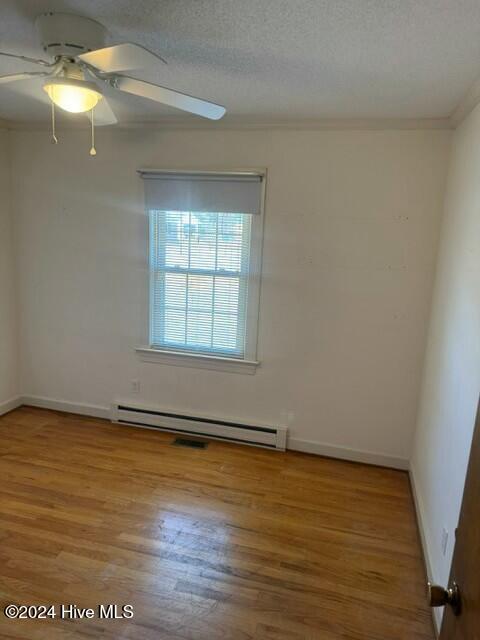 empty room with ceiling fan, baseboard heating, wood-type flooring, a textured ceiling, and ornamental molding