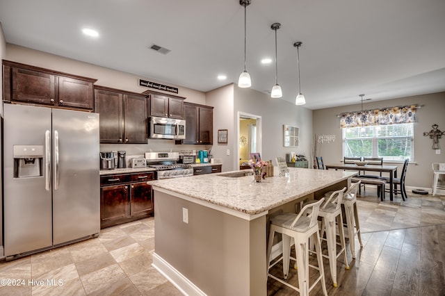 kitchen with pendant lighting, sink, an island with sink, light stone counters, and stainless steel appliances