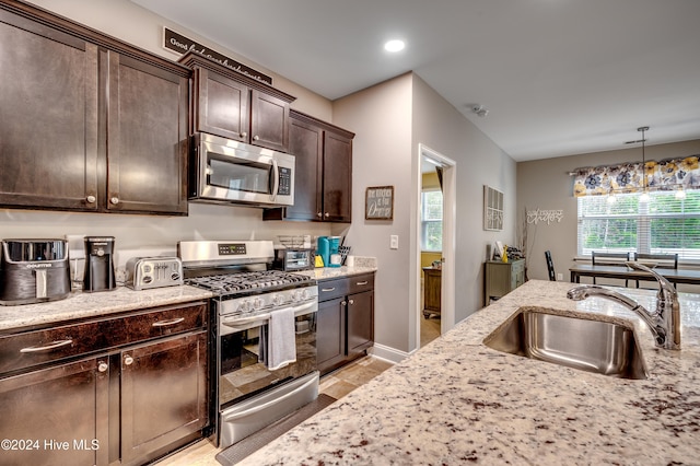 kitchen with appliances with stainless steel finishes, light stone counters, dark brown cabinets, sink, and pendant lighting