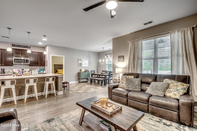 living room with ceiling fan with notable chandelier and light hardwood / wood-style flooring