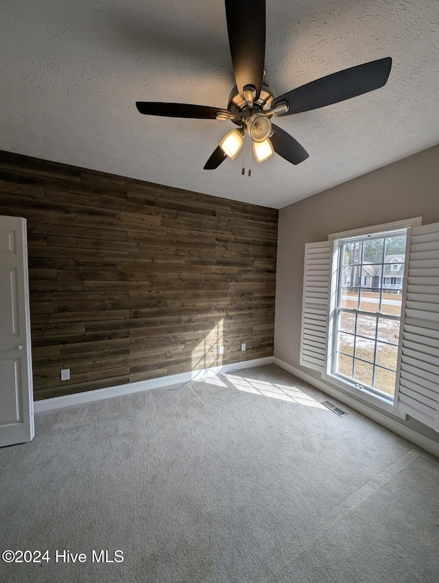 empty room featuring carpet flooring, a textured ceiling, ceiling fan, and wood walls