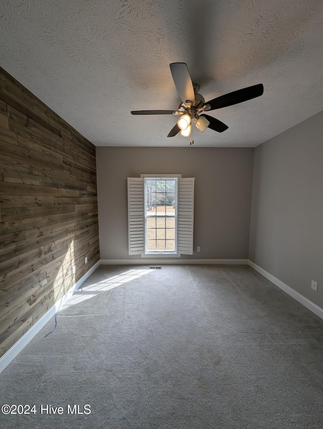 carpeted spare room featuring a textured ceiling, ceiling fan, and wooden walls