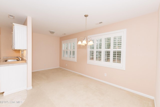 unfurnished dining area featuring sink, light colored carpet, and a chandelier