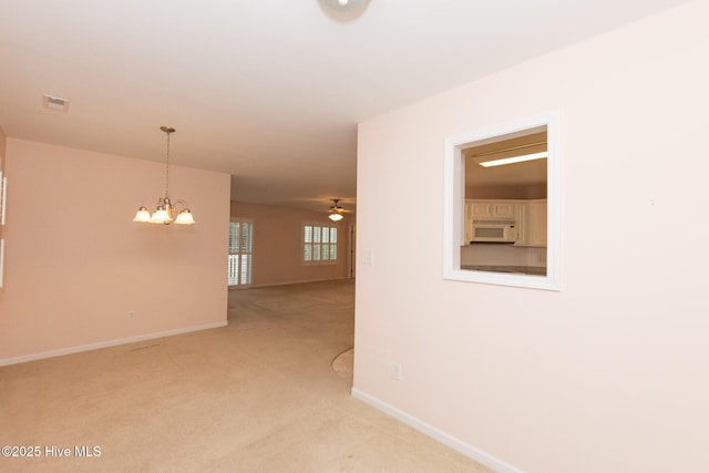 empty room featuring light carpet and ceiling fan with notable chandelier