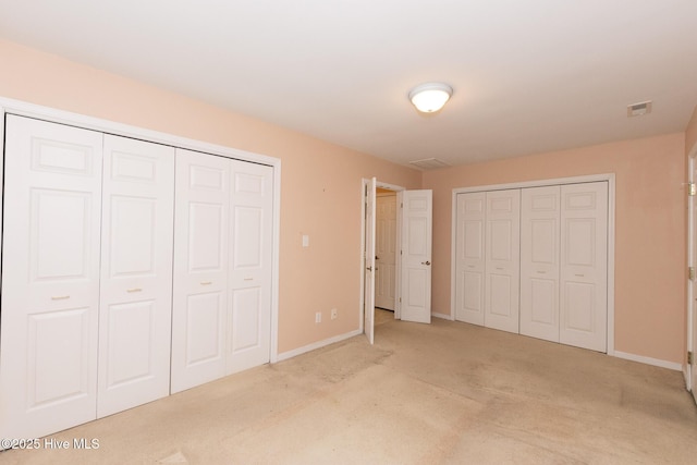 unfurnished bedroom with light colored carpet and multiple closets