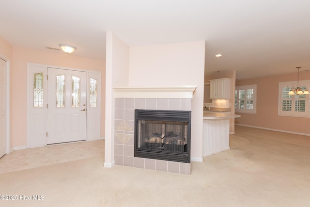 unfurnished living room featuring a tile fireplace, light colored carpet, and a notable chandelier