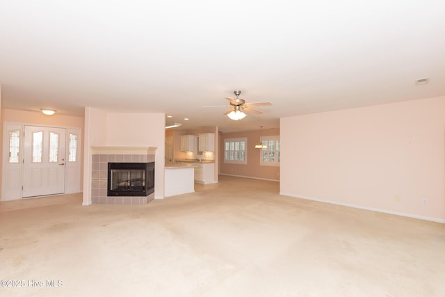 unfurnished living room featuring a tile fireplace, light colored carpet, and ceiling fan